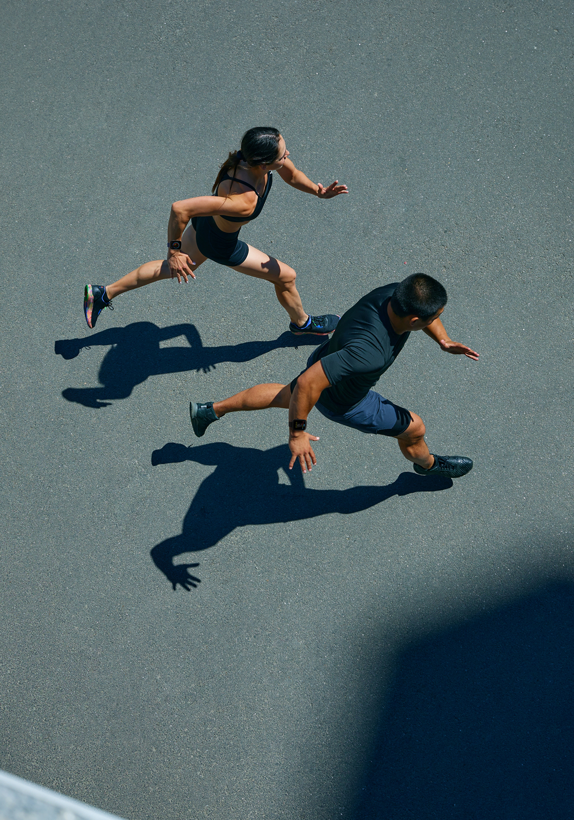 Two people running on a gray surface with shadows cast below.