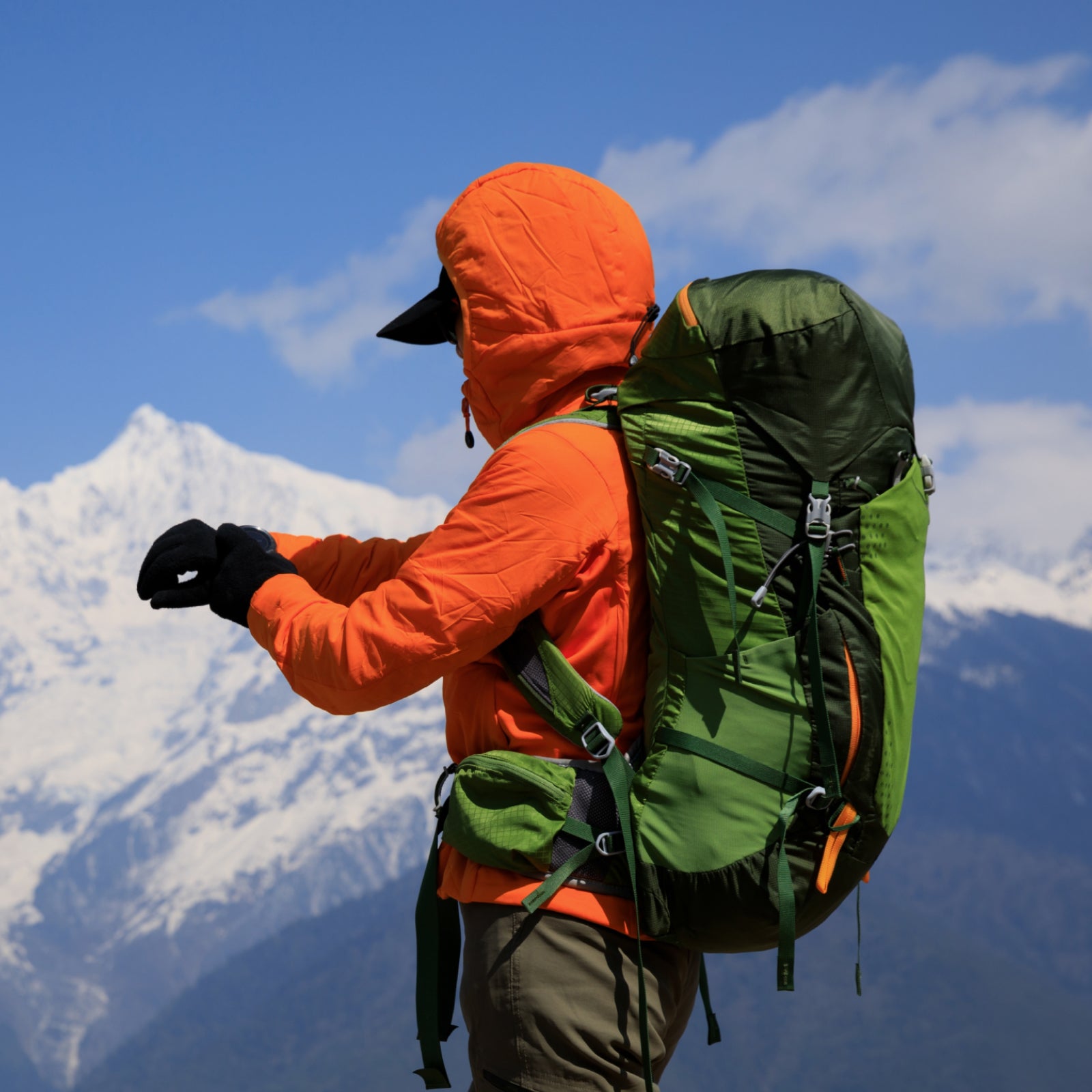 person on mountain top looking at smartwatch with backpack